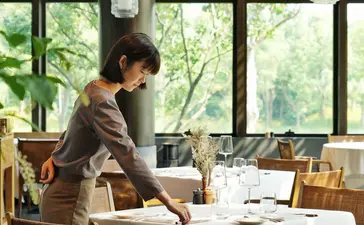 Staff member arranging dining table at Amanyangyun restaurant with garden views.