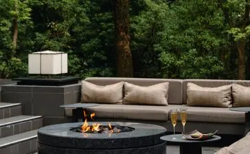 Aperitif seating area with circular fire pit at Aman Kyoto resort, surrounded by tall trees.