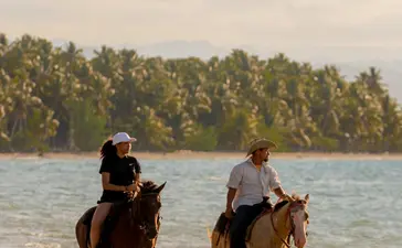 Dos jinetes a caballo en una playa tropical de Amanera resort, República Dominicana.