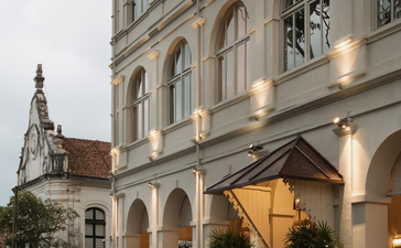 Amangalla's elegant façade at dusk, showcasing colonial architecture with illuminated ground-floor arches and a church spire beyond.