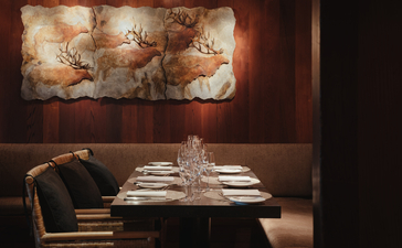 Intimate dining room at Amangani with set table and warm ambient lighting beneath artwork.
