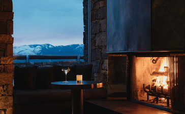 Amangani at dusk, with warm interior light glowing from stone architecture and mountains visible across the valley beyond.
