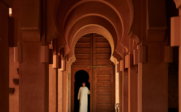 安缦珍纳度假村入口大厅，红砖拱廊两侧排列着木门，光线透过远处照亮走廊。