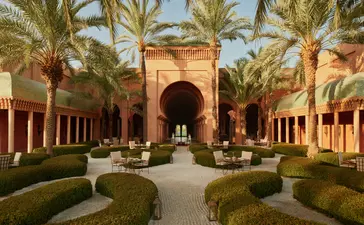 Bar extérieur d'Amanjena, resort au Maroc, avec colonnade, palmiers et bassin central.
