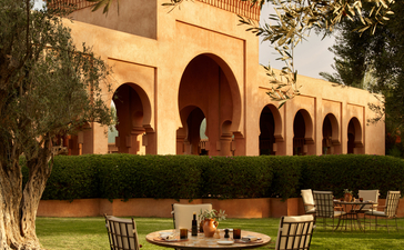 安缦珍纳度假村的摩洛哥橄榄林中，两把椅子围绕一张圆桌面向传统黄土建筑。