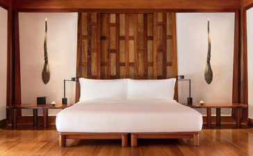 Chambre principale spacieuse d'Amanpuri avec lit blanc contemporain et panneaux bois chaud.