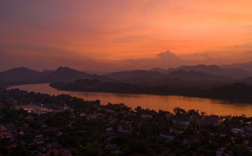 Sunset over the Mekong River at Amantaka, Laos, with golden light reflecting on the water and silhouetted hills beyond.