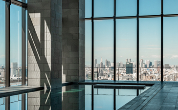 Interior swimming pool at Aman Tokyo with floor-to-ceiling windows overlooking the city skyline.