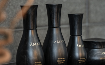 Aman Tokyo skincare bottles arranged on a dark surface with natural light casting shadows.