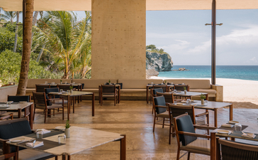Amanera resort's beachclub dining area with wooden tables, chairs and ocean views at sunset, Dominican Republic.