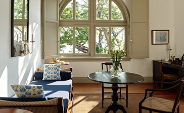 Sunlit suite at Amangalla with arched windows, wooden furniture, and seated area overlooking gardens.