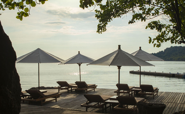 安缦湾澜度假村海滩泳池甲板，遮阳伞和躺椅面向宁静水景。