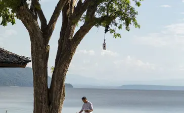 Two guests sit beneath a sprawling tree at Amanwana, overlooking the ocean and neighbouring islands in Sumbawa, Indonesia.