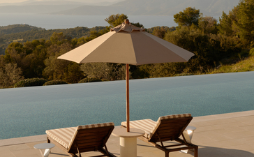 Two sun loungers beneath a parasol beside an infinity pool overlooking forested hills at Amanzoe.