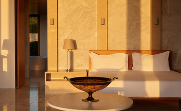 Principal bedroom at Amanzoe with warm limestone walls and minimalist furnishings bathed in golden light.