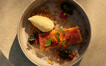 Overhead view of a dessert bowl at Amanzoe beach club restaurant, featuring caramelised cake, berries, and vanilla ice cream.