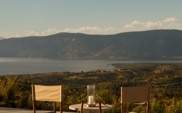 Two chairs on a terrace at Nama restaurant overlooking the Aegean Sea and mountains at Amanzoe, Greece.