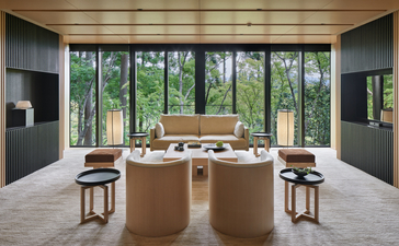Wooden kitchen island with seating in a bright, open-plan kitchen at Aman Kyoto, overlooking gardens through large windows.