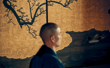 Man in profile before gold-toned artwork depicting bare branches at Aman Kyoto.