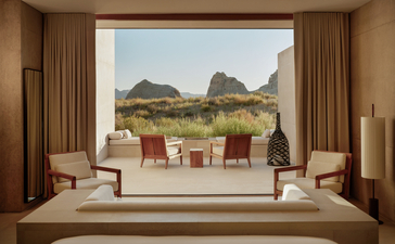 Amangiri suite with floor-to-ceiling windows framing desert rock formations and a furnished terrace beyond.