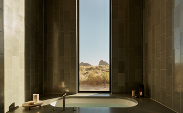 Amangiri suite with soaking tub positioned before floor-to-ceiling windows overlooking desert landscape.