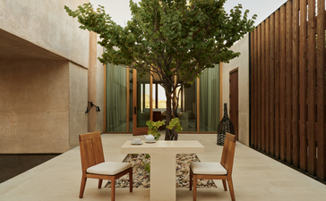 Amangiri suite with dining table, wooden chairs, and potted tree in serene interior space.