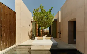 Amangiri resort desert pool suite courtyard with stone seating and green tree.