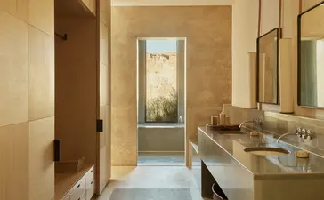 Orchard Suite bathroom at Amangiri with dual vanities, warm stone finishes, and natural light from corridor entry.