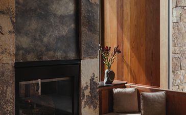 Amangani bedroom with dark stone fireplace, wooden door, and bathtub by window.