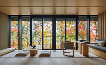 Serene interior at Aman Kyoto with sliding doors opening onto autumn foliage and traditional wooden furnishings.