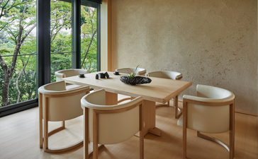 Wooden dining table and chairs at Aman Kyoto, with garden views through large windows.