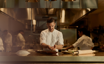 Chef preparing cuisine at Aman New York's open kitchen counter.