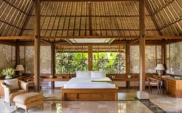 Amandari suite in Ubud with thatched roof, wooden platform bed, and open-air design overlooking tropical gardens.