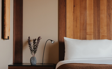 Amangani bedroom with wooden headboard panelling, white pillows and bedside table with lavender arrangement.