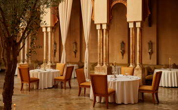 Dining courtyard at Amanjena with round tables, terracotta walls, and Moroccan architectural details.