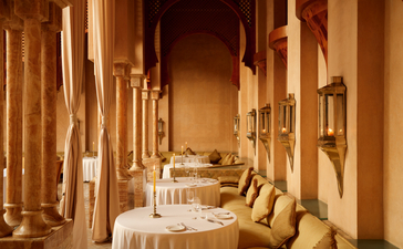 Amanjena's dining venue with ochre-coloured walls, candlelit tables, and architectural columns creating an intimate atmosphere.
