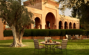 Dining area set on manicured lawn at Amanjena resort, with arched terracotta building beyond.