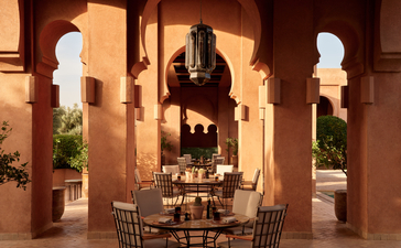 Sala da pranzo illuminata di sera presso il resort Amanjena, con archi in pietra e statue bianche.