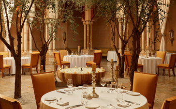 Dining table set for two at Amanjena's Moroccan restaurant, with warm lighting filtering through tall wooden columns.