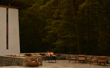 Aman Bhutan lodge exterior at dusk with wooden seating pavilion and forest backdrop, Thimphu.
