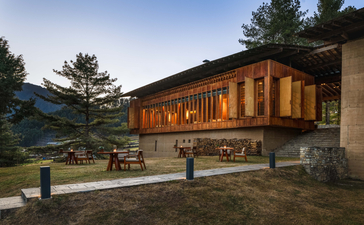 Gangtey Lodge exterior at dusk, with warm-lit windows and stone terrace overlooking Bhutanese valley.