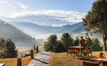 Outdoor dining area at Aman Gangtey Lodge with mountain views across the Bhutanese valley.