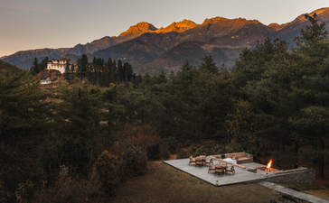 Amankora lodge exterior at dusk, with firepit terrace overlooking forested valley and mountains in Paro, Bhutan.