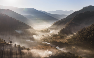 Misty mountain valley at Aman Bhutan with forested slopes and morning light filtering through clouds.