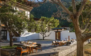 Farmhouse courtyard at Aman Bhutan Punakha with traditional architecture, mature tree, and mountain views.