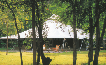 安缦湾澜度假村的草坪，透过树木可见水景和帐篷结构。