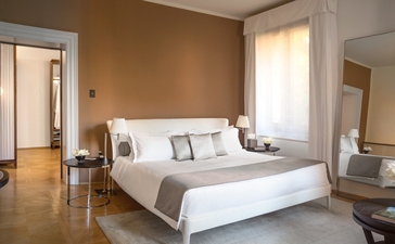 Principale camera da letto con letto bianco, pareti beige e finestre che si affacciano su Venezia presso Aman Venice.