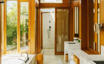 Bathroom at Amanera with wooden cabinetry, rainfall shower, and garden views through French doors.