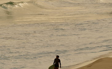 Surfer solitaire marchant vers l'océan à Amanera, resort en bord de plage.
