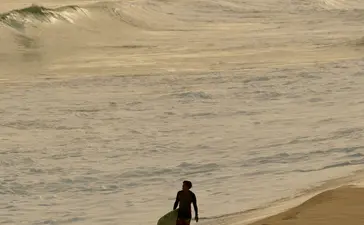 Surfer in wetsuit entering the sea at Amanera resort beach.